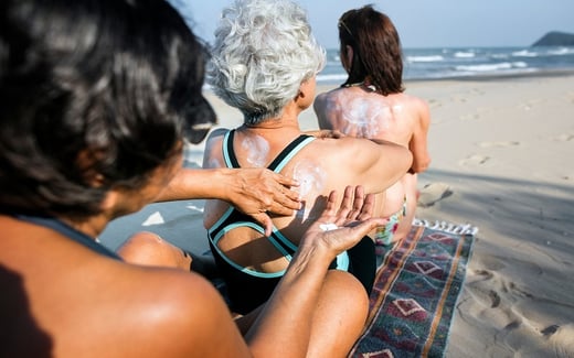 Three women at the beach applying sunscreen